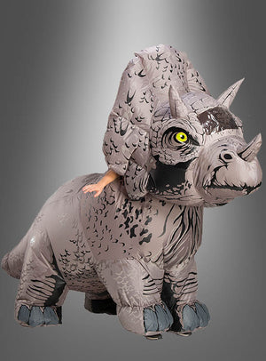 Eine Person, die ein großes, graues aufblasbares Triceratops-Kostüm aus „Jurassic World“ trägt, wobei nur ihre Arme zu sehen sind, vor einem grauen Hintergrund mit Farbverlauf.