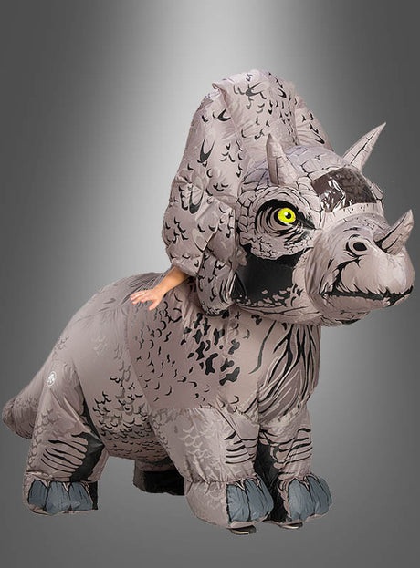 Eine Person, die ein großes, graues aufblasbares Triceratops-Kostüm aus „Jurassic World“ trägt, wobei nur ihre Arme zu sehen sind, vor einem grauen Hintergrund mit Farbverlauf.