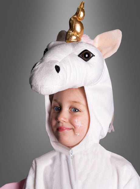 Vor einem grauen Hintergrund lächelt ein Kind, das das weiße „Zauberhaftes Plüsch-Einhorn-Kostüm Deluxe“ mit einem schimmernden goldenen Horn trägt. Auf seiner Wange sind weiße Sternchen aufgemalt – damit ist dieses zauberhafte Tierkostüm ideal für Fasching, Karneval oder Halloween.