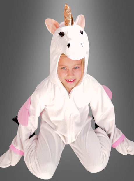 Ein Kind, das einen „Zauberhaftes Plüsch-Einhorn“-Deluxe-Strampler mit goldenem Horn und rosa Akzenten trägt, kniet vor einem grauen Hintergrund mit Farbverlauf – perfekt für Fasching, Karneval, Halloween oder als Tierkostüm für Mädchen.