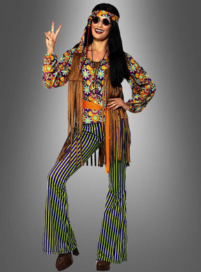 Eine Person, die das „Moonchild Hippie“-Kostüm für Damen trägt, bestehend aus einem bunten Oberteil mit Blumenmuster, gestreiften Schlaghosen, einer Fransenweste und einer runden Sonnenbrille, sowie einem Stirnband, und das Peace-Zeichen macht.