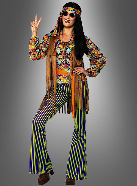 Eine Person, die das „Moonchild Hippie“-Kostüm für Damen trägt, bestehend aus einem bunten Oberteil mit Blumenmuster, gestreiften Schlaghosen, einer Fransenweste und einer runden Sonnenbrille, sowie einem Stirnband, und das Peace-Zeichen macht.