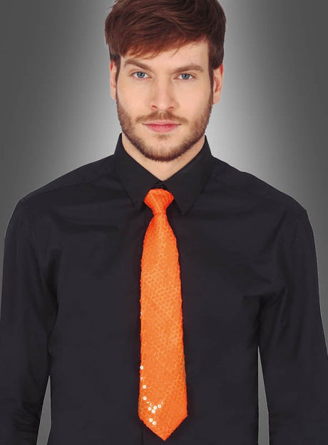 Ein Mann in einem schwarzen Hemd und einer leuchtend orangefarbenen Unisex-Paillettenkrawatte, die an ein farbenfrohes Karnevalsaccessoire erinnert, steht vor einem grauen Hintergrund mit Farbverlauf und blickt mit neutralem Gesichtsausdruck nach vorne. Die auffällige Unisex-Paillettenkrawatte verleiht seinem ansonsten zurückhaltenden Look eine verspielte Note.