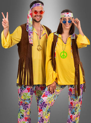 Zwei Personen in farbenfrohen Hippie-Kostümen im Stil der 1970er Jahre – darunter gelbe Hemden, Hosen mit Blumenmuster, Westen, Stirnbänder, Halsketten mit Peace-Zeichen und runde Sonnenbrillen – stehen nebeneinander, posieren und lächeln in ihrem stilvollen „Hippie-Look Bettina“-Damenkostüm.
