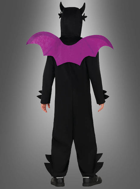 Eine Person, die einen „Schwarzer Drachen“-Overall trägt – ein schwarzes Kostüm mit angenähten violetten Fledermausflügeln, einer Kapuze mit Hörnern und spitzen Details –, steht mit dem Rücken zur Kamera vor einem grauen Hintergrund mit Farbverlauf.