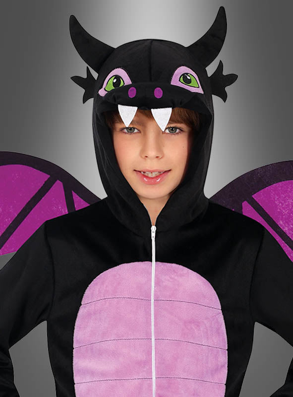 Ein Kind trägt einen „Schwarzer Drachen“-Overall in Schwarz und Lila mit Flügel- und Hornverzierungen sowie einer Kapuze mit Augen, Reißzähnen und Ohren und steht vor einem grauen Hintergrund – der ideale Karnevals-Overall für junge Drachenfans.
