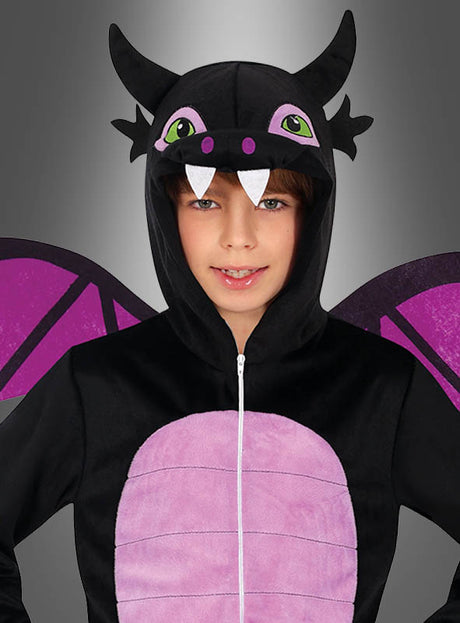 Ein Kind trägt einen „Schwarzer Drachen“-Overall in Schwarz und Lila mit Flügel- und Hornverzierungen sowie einer Kapuze mit Augen, Reißzähnen und Ohren und steht vor einem grauen Hintergrund – der ideale Karnevals-Overall für junge Drachenfans.