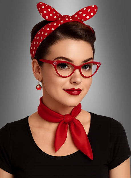 Eine Frau mit kurzen, dunklen Haaren präsentiert das Rockabilly-Set im Stil der 50er Jahre, bestehend aus einem roten Stirnband mit Polka-Dots, einer roten Brille, einem roten Schal, einem schwarzen Oberteil und roten Ohrringen – und zeigt damit vor einem neutralen Hintergrund einen stilvollen Vintage-Look.