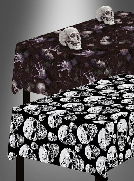 Zwei rechteckige Tische mit Tischdecken im Halloween-Stil: Auf dem einen liegt die Mehrweg-Tischdecke „Totenköpfe abwischbar“ mit Totenköpfen und Händen auf dunklem Hintergrund, auf dem anderen ein „Totenkopf-Muster“ mit weißen Totenköpfen auf schwarzem Hintergrund. Auf dem ersten Tisch liegen zwei künstliche Totenköpfe, die die perfekte Halloween-Tischdekoration abrunden.