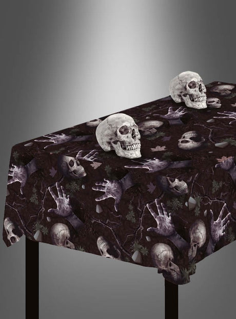 Der Tisch ist mit der abwischbaren Mehrweg-Tischdecke „Totenköpfe“ bedeckt, die ein auffälliges Totenkopfmuster mit Skeletthänden und Knochenmotiven aufweist – die perfekte Halloween-Tischdekoration. Darauf sind zwei realistische Totenkopf-Dekorationen platziert.