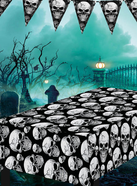 Auf einem nebligen Friedhof steht ein Tisch, der mit der abwischbaren Mehrweg-Tischdecke „Totenköpfe“ gedeckt ist; darüber sind Girlanden mit Totenkopf-Motiven angebracht, und im Hintergrund ist der Tisch von kahlen Bäumen und Grabsteinen umgeben.