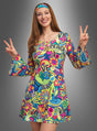 Eine Frau lächelt vor einem grauen Hintergrund mit Farbverlauf. Sie trägt das „Hippie Kleid Peace & Love“ – ein farbenfrohes, von den 1960er Jahren inspiriertes Kleid mit bunten Flower-Power-Mustern und ikonischen Peace-&-Love-Symbolen – und streckt beide Hände zum Peace-Zeichen aus.