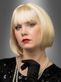 Eine Frau präsentiert die hochwertige Pagenschnitt-Bob-Perücke „Vera“ mit kurzem blondem Haar im klassischen Bob-Stil. Sie trägt ein schwarzes Oberteil und schwarze Handschuhe, dazu eine Perlenkette und roten Lippenstift, und posiert vor einem grauen Hintergrund mit Farbverlauf.