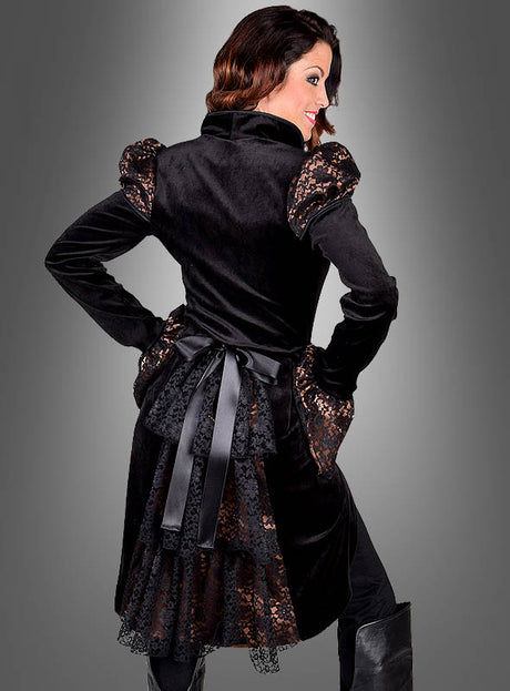 Eine Frau steht mit dem Rücken zur Kamera und trägt die Steampunk-Jacke „Lady Herriet“ aus schwarzem Samt mit Spitzendetails, Puffärmeln, einer Schleife am Rücken und Spitzenbesatz im typisch viktorianischen Stil vor einem schlichten grauen Hintergrund.