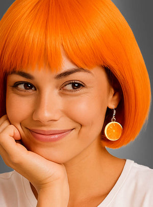 Eine lächelnde Person mit einem leuchtend orangefarbenen Bob-Haarschnitt trägt die „Orangen Ohrringe Scheibe“ – einen Ohrring in Form einer Orangenscheibe –, während sie ihr Kinn auf die Hand stützt; sie trägt ein weißes Hemd vor einem grauen Hintergrund.