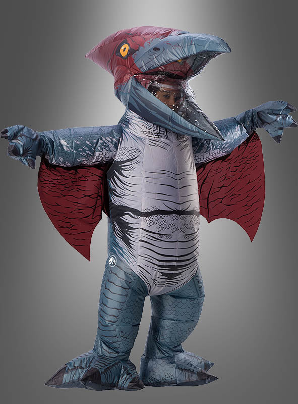 Eine Person trägt ein blau-rotes, aufblasbares Pteranodon-Kostüm mit ausgebreiteten Flügeln und steht vor einem schlichten grauen Hintergrund.