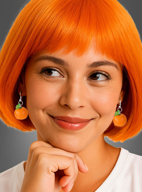 Eine Frau mit einem leuchtend orangefarbenen Bob-Haarschnitt lächelt, die Hand unter dem Kinn, und trägt die markanten Ohrringe „Orangen Ohrringe Scheibe oder ganze Frucht“ in Form von Früchten vor einem neutralen grauen Hintergrund.