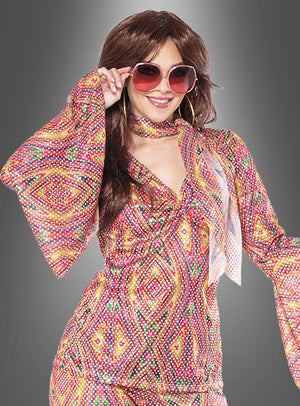 Eine Person trägt einen bunten Disco-Anzug mit Pailletten für Damen mit Schlaghose und einer großen Sonnenbrille und posiert, wobei sie die Brille mit einer Hand vor einem grauen Hintergrund mit Farbverlauf hält.