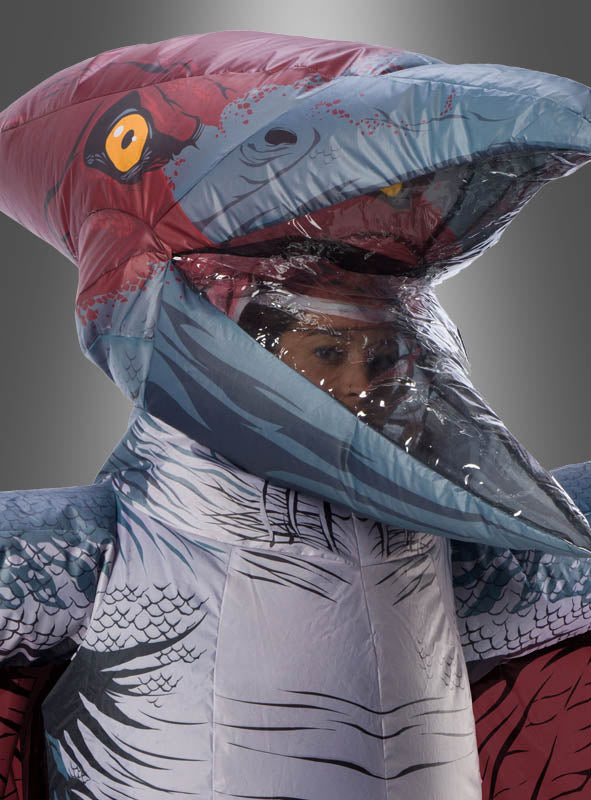 Eine Person, die ein aufblasbares Pteranodon-Kostüm mit einem transparenten Einsatz trägt, durch den ihr Gesicht zu sehen ist, vor einem schlichten grauen Hintergrund – ein lustiges und auffälliges aufblasbares „Jurassic World“-Kostüm für jeden Dino-Fan.