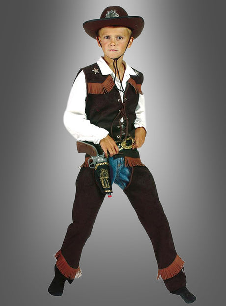 Ein kleiner Junge trägt das Western-Cowboy-Kostüm für Kinder, bestehend aus Hut, Weste, weißem Hemd, Chaps und einer Spielzeugpistole, während er vor einem schlichten grauen Hintergrund steht.