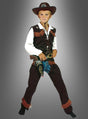 Ein kleiner Junge trägt das Western-Cowboy-Kostüm für Kinder, bestehend aus Hut, Weste, weißem Hemd, Chaps und einer Spielzeugpistole, während er vor einem schlichten grauen Hintergrund steht.