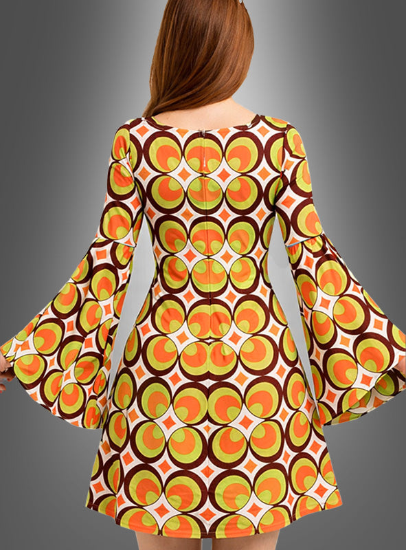 Vor einem grauen Hintergrund ist eine Frau mit langen Haaren von hinten zu sehen. Sie trägt das waschbare 70er-Jahre-Retro-Kleid „Nicky“ mit orangefarbenen, gelben und braunen geometrischen Mustern und ausgestellten Ärmeln. Das auffällige 70er-Jahre-Muster macht dieses Kleid zu einem idealen Kostüm für Mottopartys im Vintage-Stil.