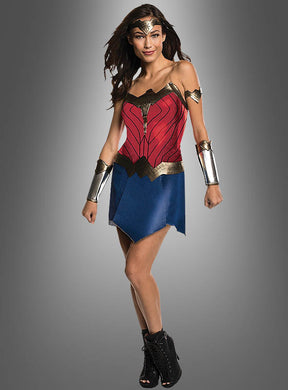 Eine Person, die das „Wonder Woman für Damen“-Kostüm aus „Justice League“ trägt – bestehend aus einem roten Oberteil, einem blauen Rock, Armbanden, einer Tiara und schwarzen Stiefeln –, steht vor einem grauen Hintergrund.