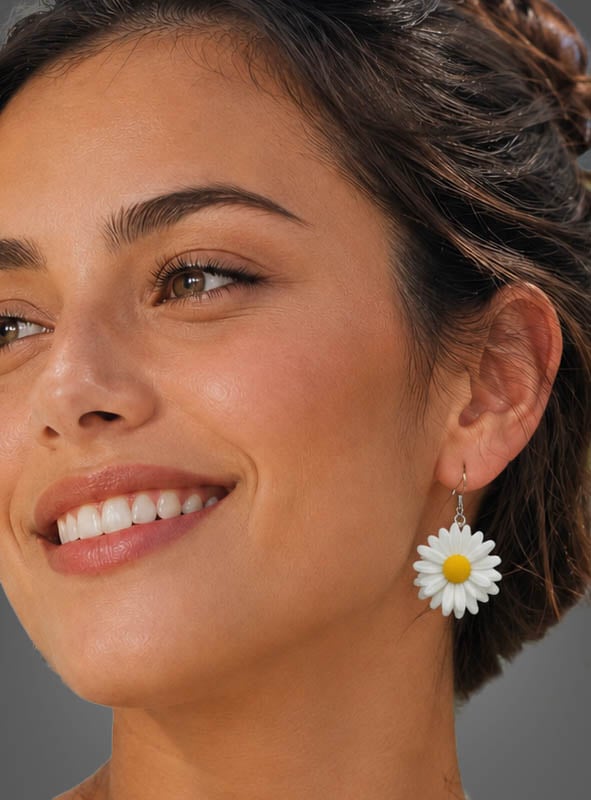 Eine Frau mit braunen Haaren lächelt und trägt die „Blumen Ohrringe Flower Power“ – große, gänseblümchenförmige Ohrringe mit weißen Blütenblättern und einer gelben Mitte –, die den Boho-Look und die Flower-Power-Stimmung perfekt verkörpern.