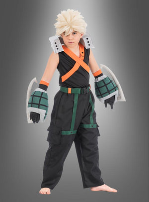 Ein Kind steht barfuß vor einem grauen Hintergrund und trägt das Katsuki-Bakugo-Kostüm für Kinder aus „My Hero Academia“ – mit einer stacheligen blonden Perücke, einem schwarzen Kostüm mit orangefarbenen Trägern, großen grauen Handschuhen und grünen Details – ideal für jeden jungen Fan, der einen authentischen Look sucht.