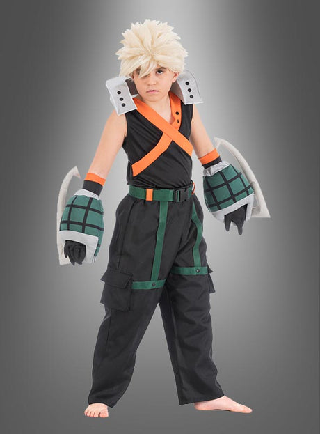 Ein Kind steht barfuß vor einem grauen Hintergrund und trägt das Katsuki-Bakugo-Kostüm für Kinder aus „My Hero Academia“ – mit einer stacheligen blonden Perücke, einem schwarzen Kostüm mit orangefarbenen Trägern, großen grauen Handschuhen und grünen Details – ideal für jeden jungen Fan, der einen authentischen Look sucht.