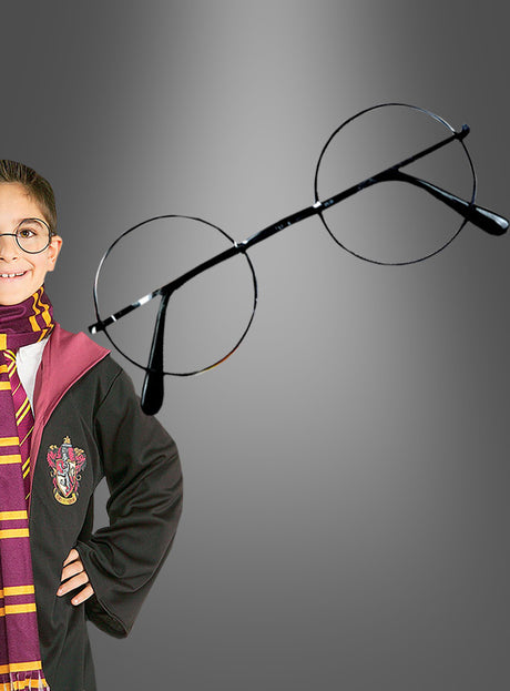 Ein Kind in einer schwarzen Robe und einem gestreiften Schal steht vor einem grauen Hintergrund neben der runden Harry-Potter-Brille zum Kostüm – perfekt, um ein Harry-Potter-Kostüm oder eine Hogwarts-Schuluniform zu vervollständigen.