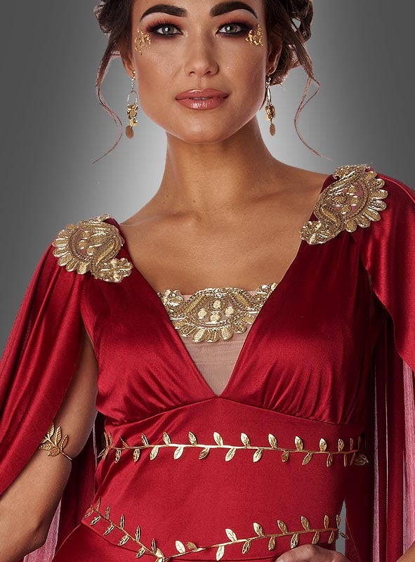 Eine Frau, gekleidet als die griechische Göttin der Morgenröte Eos, in einem roten Kleid, das mit goldenen Verzierungen und zarten Blattmotiven geschmückt ist, die an antike Göttinnen erinnern, ergänzt durch goldene Ohrringe und passende dekorative Akzente im Gesicht, vor einem grauen Hintergrund mit Farbverlauf.