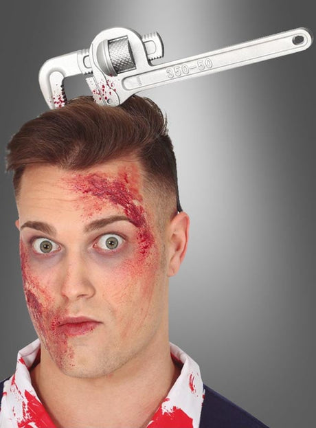 Ein Mann mit Kunstblut im Gesicht trägt einen Halloween-Kopfschmuck – einen „Horror-Haarreif mit Werkzeugen im Kopf“, der den Anschein erweckt, als würde ein großer Schraubenschlüssel durch seinen Kopf ragen.