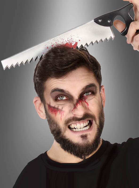 Ein Mann mit blutähnlicher Gesichtsbemalung hält eine Requisitensäge in der Hand, die scheinbar durch seinen Kopf geht, und sorgt so für einen dramatischen Halloween-Effekt, der durch den Horror-Haarreif „Werkzeuge im Kopf“ ergänzt wird, der den gruseligen Look noch verstärkt.