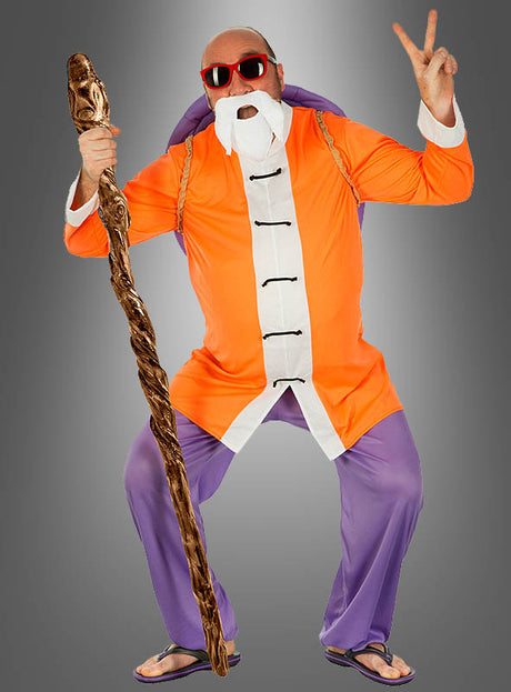 Eine Person, die das „Dragon Ball Z“-Kostüm „Muten-Roshi“ trägt – komplett mit weißem Bart, Sonnenbrille und einem Stab –, posiert vor einem grauen Hintergrund und formt dabei mit einer Hand das Peace-Zeichen.