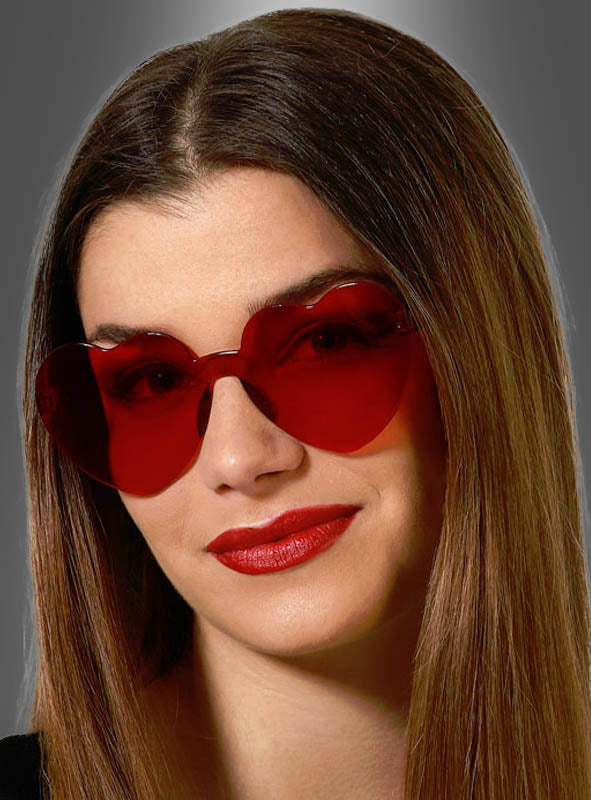 Eine Frau mit glattem braunem Haar trägt eine auffällige rote Herzbrille zum Karnevalskostüm und knallroten Lippenstift vor einem schlichten grauen Hintergrund – ein ideales Accessoire für den Karneval oder jede andere festliche Veranstaltung.