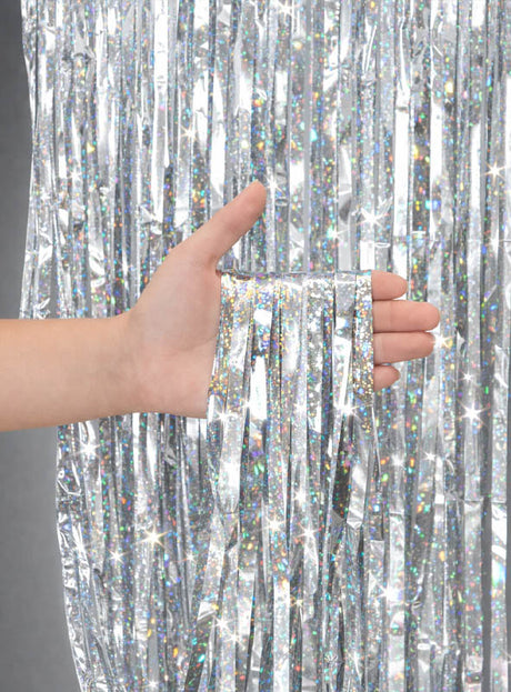 Eine Hand hält mehrere Stränge glänzender silberner Lametta vor einem passenden Lametta-Hintergrund – damit eignet sich der „Glitter Lametta Vorhang“ (100 x 250 cm) perfekt, um bei Ihrer nächsten Feier eine auffällige „Glitzervorhang“-Partydekoration zu gestalten.