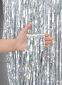Eine Hand hält mehrere Stränge glänzender silberner Lametta vor einem passenden Lametta-Hintergrund – damit eignet sich der „Glitter Lametta Vorhang“ (100 x 250 cm) perfekt, um bei Ihrer nächsten Feier eine auffällige „Glitzervorhang“-Partydekoration zu gestalten.