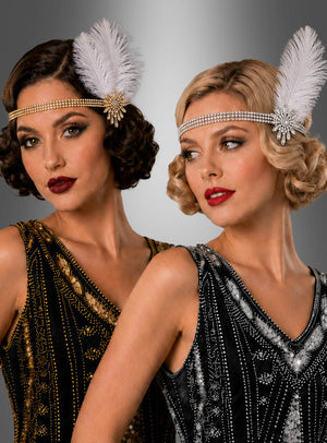 Zwei Frauen tragen mit Perlen bestickte Flapper-Kleider im Stil der 1920er Jahre und dazu Strass-Haarschmuck mit Federn aus den 20er Jahren; sie posieren nebeneinander vor einem grauen Hintergrund mit Farbverlauf.