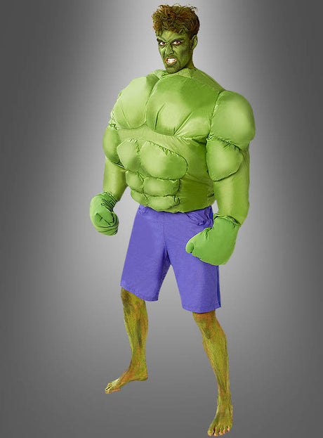 Ein Mann posiert vor einem grauen Hintergrund mit Farbverlauf und trägt das aufblasbare Hulk-Kostüm für Herren, bestehend aus lila Shorts und passenden Handschuhen.