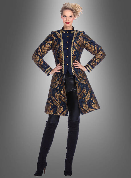 Vor einem schlichten grauen Hintergrund steht eine Frau, die eine lange, marineblaue „Luxus Barock Brokat Jacke Damen“ mit Goldstickerei trägt, dazu schwarze Hosen und schwarze Stiefel mit hohen Absätzen.