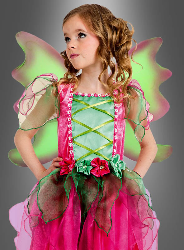 Ein junges Mädchen mit lockigem Haar und Blumenverzierungen posiert vor einem grauen Hintergrund und trägt das „Zauberhaftes Feenkostüm für Mädchen“ – ein zauberhaftes rosa-grünes Feenkleid mit zarten Flügeln.