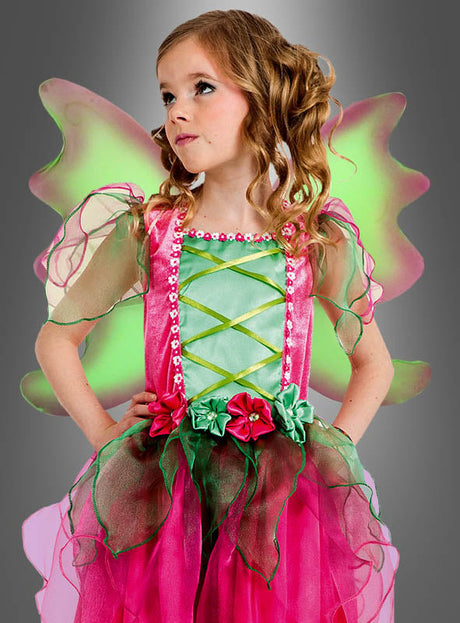 Ein junges Mädchen mit lockigem Haar und Blumenverzierungen posiert vor einem grauen Hintergrund und trägt das „Zauberhaftes Feenkostüm für Mädchen“ – ein zauberhaftes rosa-grünes Feenkleid mit zarten Flügeln.