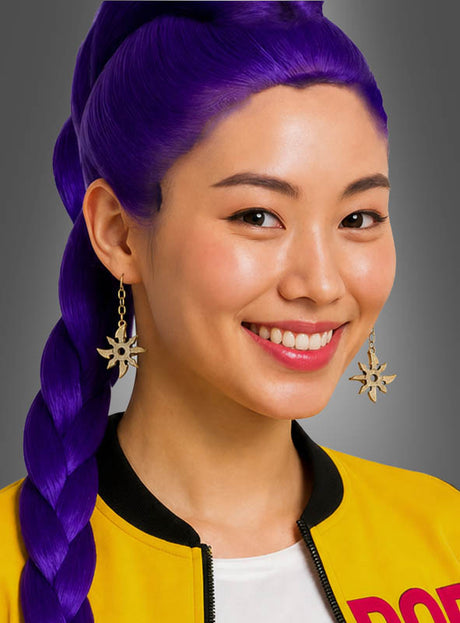 Eine Frau mit langen, zu Zöpfen geflochtenen violetten Haaren, die auffällige Ninja-Wurfsterne-Ohrringe im asiatischen Stil, eine gelbe Jacke und ein weißes Hemd trägt, lächelt vor einem grauen Hintergrund in die Kamera.