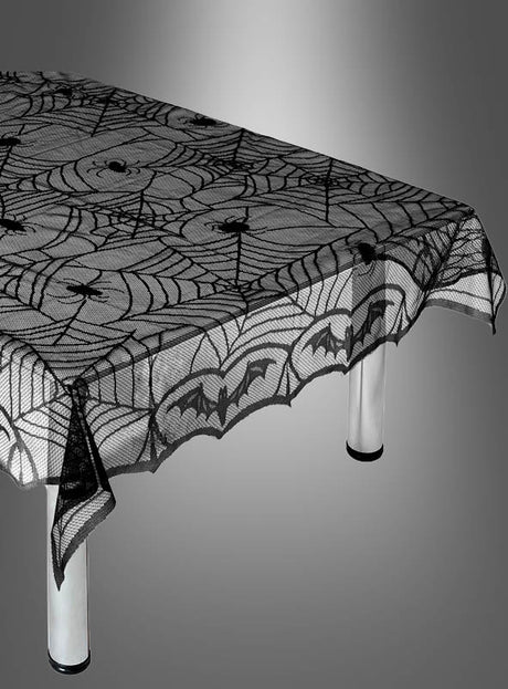 Ein Tisch, der mit einer „Halloween-Tischdecke“ bedeckt ist – einer wiederverwendbaren schwarzen Spitzentischdecke mit Spinnennetz-, Spinnen- und Fledermausmotiven auf einfarbigem Hintergrund.