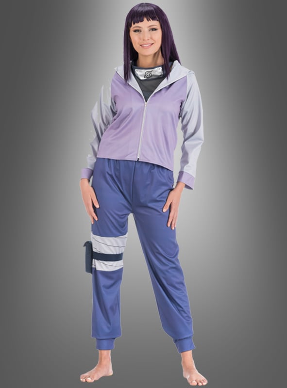 Eine Person steht barfuß und lächelt. Sie trägt ein lila Hinata-Kostüm für Erwachsene aus Naruto mit einer Jacke, einem Ninja-Stirnband und Schienbeinschützern vor einem schlichten grauen Hintergrund.