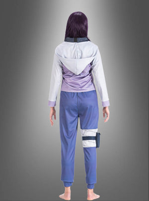 Eine Person in einem lila-weißen Kapuzenpulli und einer blauen Hose steht barfuß mit dem Rücken zum Betrachter vor einem grauen Hintergrund mit Farbverlauf und erinnert damit an das Hinata-Kostüm für Erwachsene aus Naruto.