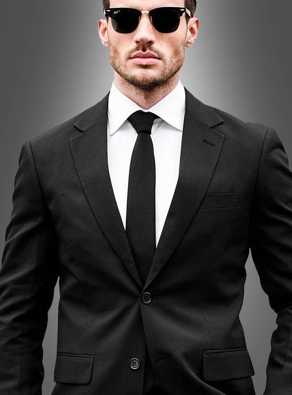 Ein Mann, der einen schwarzen Anzug von OppoSuits, ein weißes Hemd, eine schwarze Krawatte und eine Sonnenbrille trägt, steht vor einem grauen Hintergrund.