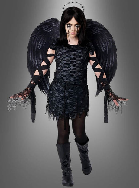 Ein Mädchen trägt das „Schwarzer Engel“-Kostüm für Mädchen mit schwarzen Flügeln, Heiligenschein, schwarzen Handschuhen und schwarzen Make-up-Streifen unter den Augen vor grauem Hintergrund – das ideale Kinderkostüm für Halloween.