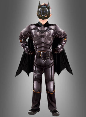 Ein Kind steht mit den Händen in den Hüften und trägt das Batman Original Kinderkostüm – komplett mit Umhang und Maske – und blickt selbstbewusst vor sich hin vor einem grauen Hintergrund. Dieses auffällige DC Comics-Lizenzkostüm fängt den ikonischen Superhelden-Look für jeden jungen Fan perfekt ein.